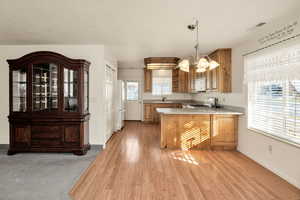 Kitchen with a peninsula, hanging light fixtures, light countertops, light wood-type flooring, and white appliances