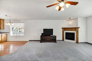 Unfurnished living room with ceiling fan, a fireplace, light carpet, and a chandelier