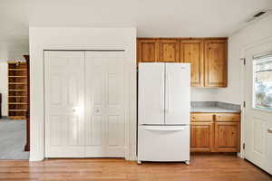 Kitchen with freestanding refrigerator, brown cabinets, light countertops, and light wood-style floors