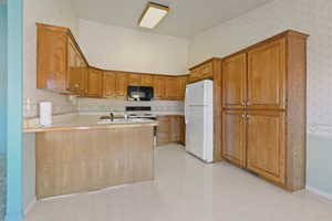 Kitchen with wallpapered walls, a peninsula, a freestanding refrigerator, light countertops, and microwave, a dishwasher, range.