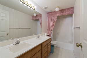 Bathroom with double vanity, wallpapered walls, a textured ceiling, and shower / bath combo