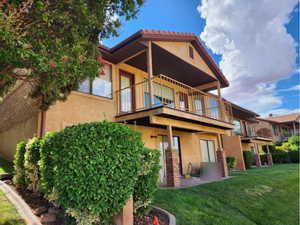 Back of property with stucco siding, a balcony, a lawn, and a patio area