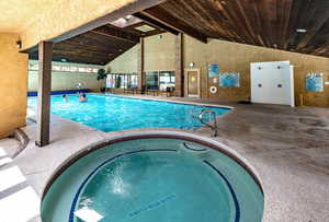 Indoor community pool with a patio area and a hot tub