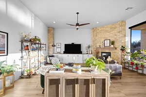 Living room with a stone fireplace, light wood-type flooring, ceiling fan, and recessed lighting