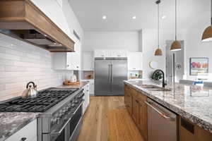 Kitchen featuring high end appliances, pendant lighting, custom exhaust hood, decorative backsplash, and brown cabinets