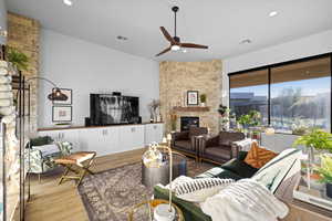 Living room with a stone fireplace, light wood-style floors, ceiling fan, and recessed lighting