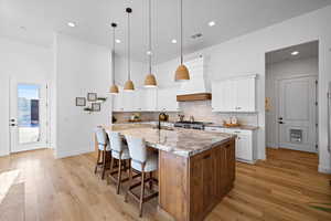 Kitchen with white cabinets, a breakfast bar area, an island with sink, light wood finished floors, and recessed lighting