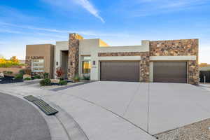 View of front facade with stone siding, driveway, stucco siding, and an attached garage