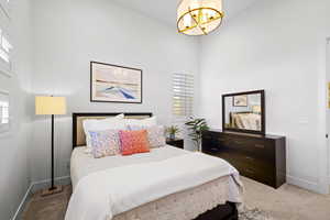 Bedroom featuring light colored carpet, a chandelier, and a towering ceiling