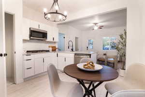 Kitchen featuring white cabinets, a peninsula, light wood-style floors, stainless steel appliances, and a chandelier