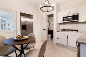 Kitchen featuring appliances with stainless steel finishes, light wood finished floors, white cabinetry, and a chandelier