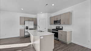 Kitchen featuring appliances with stainless steel finishes, an island with sink, dark wood-style floors, recessed lighting, and light stone counters