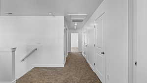 Corridor featuring dark colored carpet, an upstairs landing, attic access, and a textured ceiling