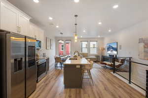 Kitchen with stainless steel appliances, an island with sink, decorative light fixtures, a breakfast bar, and light wood-type flooring