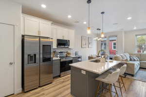 Kitchen featuring appliances with stainless steel finishes, open floor plan, white cabinetry, tasteful backsplash, and an island with sink