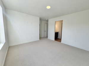 Unfurnished bedroom featuring light colored carpet, ensuite bath, and a textured ceiling