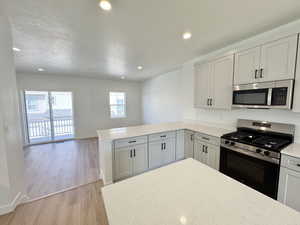 Kitchen featuring stainless steel appliances, recessed lighting, light wood-style flooring, a peninsula, and a textured ceiling