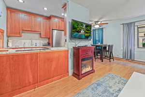 Kitchen with backsplash, light wood-type flooring, freestanding refrigerator, light stone counters, and recessed lighting