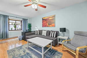 Living area featuring light wood-style flooring, ceiling fan, and a baseboard radiator