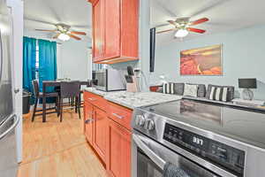 Kitchen with ceiling fan, appliances with stainless steel finishes, light stone counters, and light wood finished floors