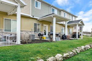 Rear view of property with a patio, stone siding, and a lawn