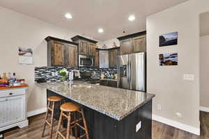 Kitchen with dark brown cabinets, stainless steel appliances, light stone countertops, decorative backsplash, and a peninsula