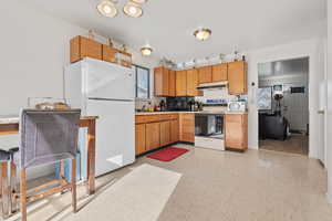 Kitchen featuring white appliances, light countertops, light floors, brown cabinets, and healthy amount of natural light