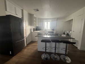 Kitchen with white cabinetry, appliances with stainless steel finishes, a kitchen island, dark wood-type flooring, and a textured ceiling