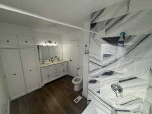 Bathroom with double vanity, dark wood-style flooring, and tiled shower
