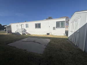 Rear view of house with a storage unit and a lawn