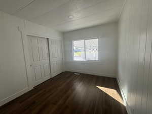 Unfurnished bedroom with dark wood-style floors, wood walls, and a closet