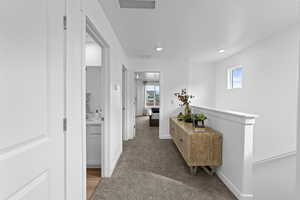 Hall with healthy amount of natural light, light colored carpet, an upstairs landing, and recessed lighting