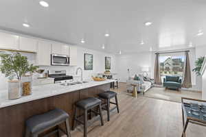 Kitchen featuring white cabinetry, stainless steel appliances, a kitchen bar, light wood-style floors, and recessed lighting