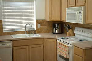 Kitchen featuring white appliances, light brown cabinetry, light countertops, and tasteful backsplash