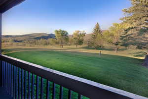 View of grassy yard featuring a balcony, a mountain view, and a view of countryside