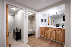 Bathroom featuring vanity, a textured ceiling, washtub / shower combination, and light wood-style floors