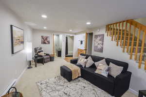 Living room with light colored carpet, a baseboard heating unit, recessed lighting, stairs, and a textured ceiling