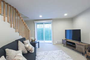 Carpeted living area featuring a baseboard heating unit, recessed lighting, and stairs