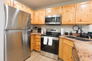 Kitchen featuring stainless steel appliances, light brown cabinetry, light stone countertops, and light wood-type flooring