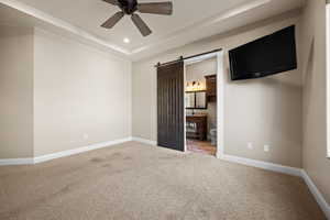 Unfurnished bedroom with a barn door, carpet flooring, a raised ceiling, a ceiling fan, and ensuite bath