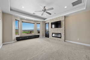 Unfurnished living room featuring a raised ceiling, light colored carpet, a ceiling fan, a large fireplace, and recessed lighting