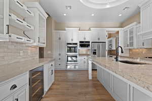 Kitchen with glass insert cabinets, white cabinets, tasteful backsplash, wine cooler, and stainless steel appliances