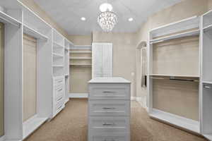 Walk in closet featuring a chandelier, light carpet, and arched walkways