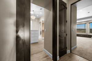 Hallway featuring light colored carpet, arched walkways, light wood-style flooring, a chandelier, and recessed lighting