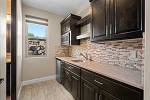 Kitchen with open shelves, backsplash, dark brown cabinetry, light wood-style flooring, and appliances with stainless steel finishes