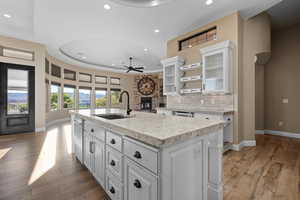 Kitchen featuring glass insert cabinets, white cabinets, light stone counters, a fireplace, and ceiling fan