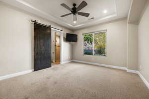 Unfurnished bedroom with light colored carpet, a barn door, a tray ceiling, ceiling fan, and recessed lighting