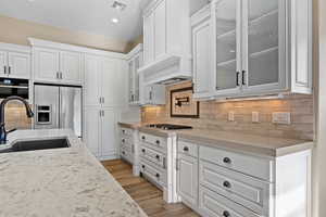 Kitchen featuring white cabinetry, glass insert cabinets, backsplash, appliances with stainless steel finishes, and light stone countertops