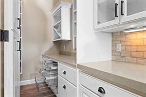 Kitchen with white cabinetry, dark wood-style flooring, decorative backsplash, light stone countertops, and glass insert cabinets