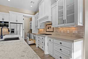 Kitchen featuring white cabinetry, backsplash, glass insert cabinets, light stone countertops, and recessed lighting